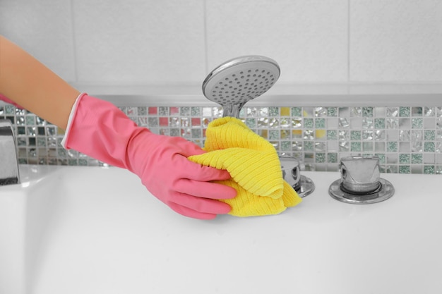 Main féminine avec pomme de douche de nettoyage de chiffon dans la salle de bain