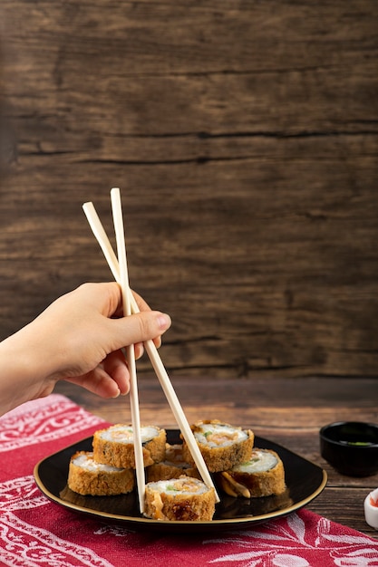 Photo main féminine prenant un rouleau de sushi chaud avec des baguettes sur une surface en bois.