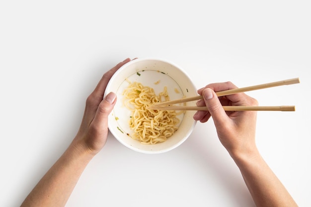 La main féminine prend des nouilles chinoises avec des baguettes chinoises à partir d'un bol en papier sur un fond blanc