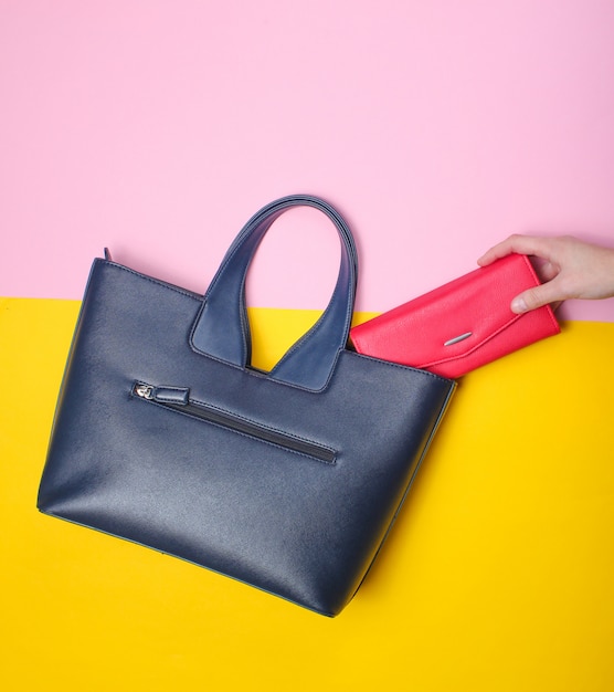 Photo la main féminine prend le portefeuille rouge du sac en cuir sur pastel. vue de dessus, pose à plat