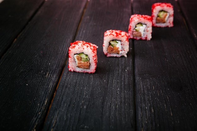 La main féminine prend des rouleaux de sushi californiens avec des baguettes chinoises mise au point sélective fond noir