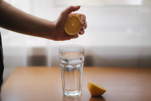 Main féminine presser le jus de citron dans un verre avec de l'eau eau avec boisson fraîche au citron en quarantaine