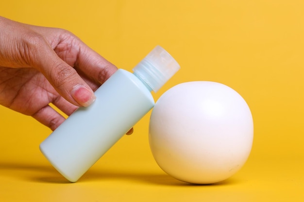 Main féminine saisissant une bouteille blanche de crème pour le corps avec un espace vide pour votre étiquette près de la sphère blanche sur