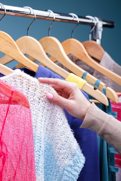 Main féminine sélectionne de nouveaux vêtements colorés sur des cintres en bois sur une grille en magasin, gros plan. Concept d'achat