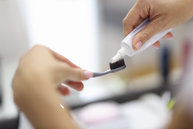 Main féminine serrant le dentifrice du tube sur la brosse à dents close up