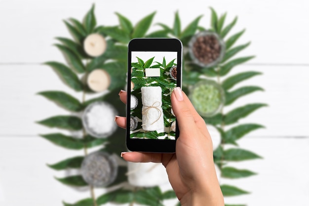 La main féminine avec un smartphone fait une photo des bocaux en verre avec un gommage corporel aux ingrédients