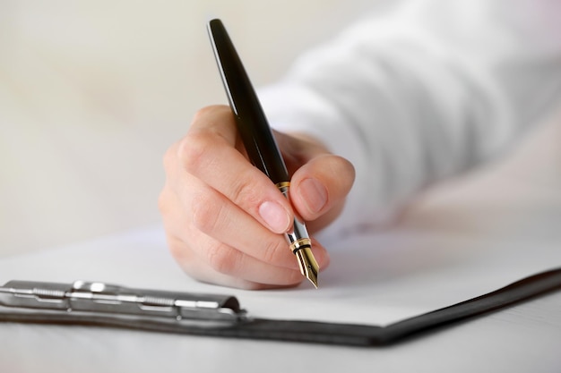 Main féminine avec stylo écrit sur papier sur le lieu de travail