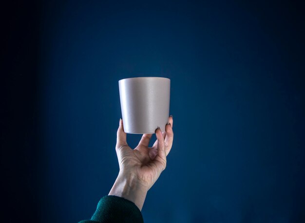 Main féminine avec une tasse sur fond bleu