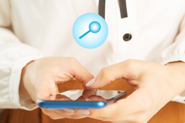 Main féminine avec téléphone portable et icônes d'une loupe, concept de recherche sur Internet via smartphone