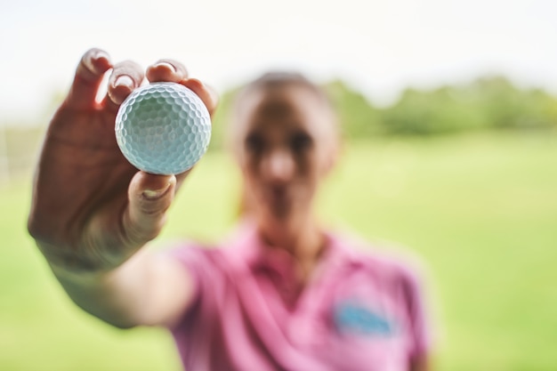 Photo main féminine tenant une balle de golf blanche devant la caméra