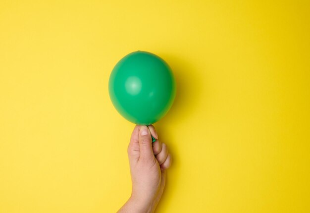 Main féminine tenant un ballon d'air vert gonflé sur un fond jaune de près