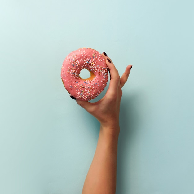 Main Féminine Tenant Un Beignet Sucré Sur Fond Bleu. Vue De Dessus, Plat Poser.