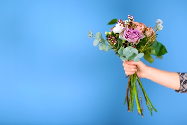 Main féminine tenant un bouquet de roses sur fond bleu