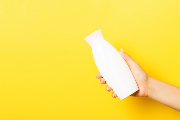 Main féminine tenant une bouteille de crème de lotion isolée. Fille donne des produits cosmétiques tube sur jaune