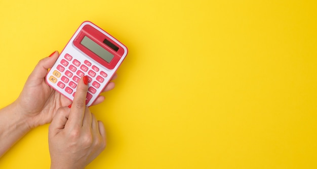 Main féminine tenant une calculatrice rose sur une surface jaune, espace de copie, bannière