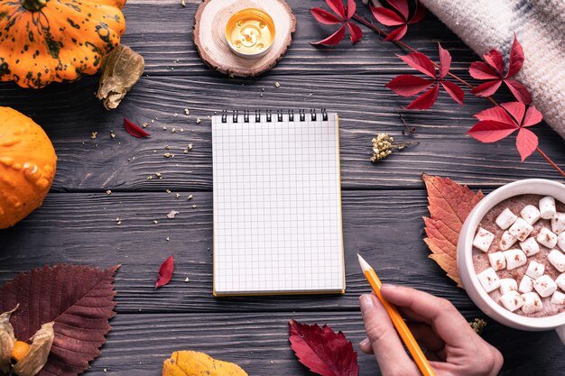 Photo main féminine tenant un crayon écrire dans un cahier maquette sur fond d'automne