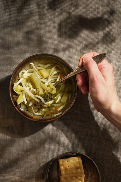 Main féminine tenant une cuillère mangeant une soupe végétarienne avec des nouilles