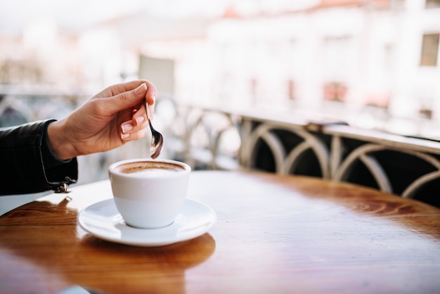 Main féminine tenant une cuillère près de la tasse à café en plein air.