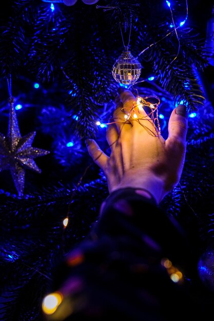 Main féminine tenant des décorations d'arbre de Noël dans la nuit. Lumière bleue de guirlande lumineuse. Moments magiques du nouvel an. Conte de fée. Magie de Noël