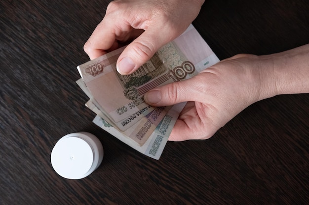 Main féminine tenant une liasse de billets roubles russes gros plan et pilules sur fond noir pauvreté