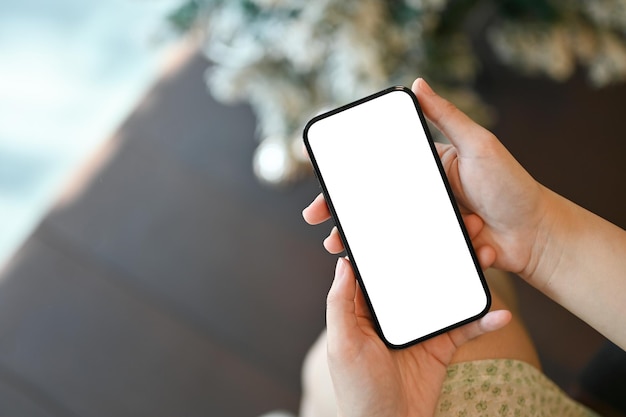 Une main féminine tenant une maquette d'écran blanc de smartphone sur fond flou