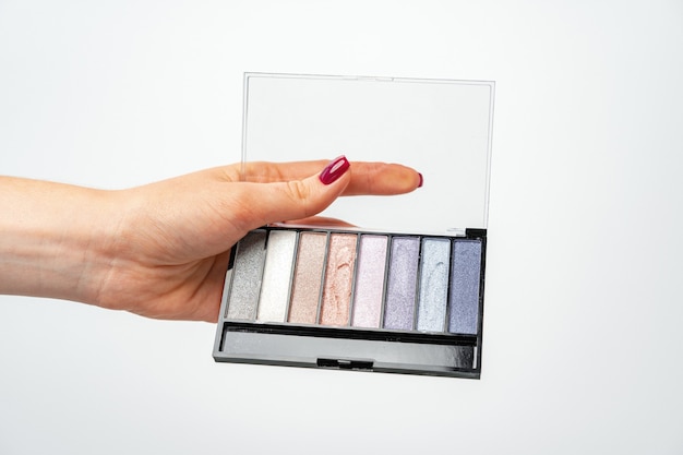 Main féminine tenant la palette de maquillage sur fond blanc close up