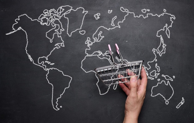 Une main féminine tenant un panier vide miniature dans le contexte d'une carte du monde dessinée Concept d'achats en ligne d'expédition internationale