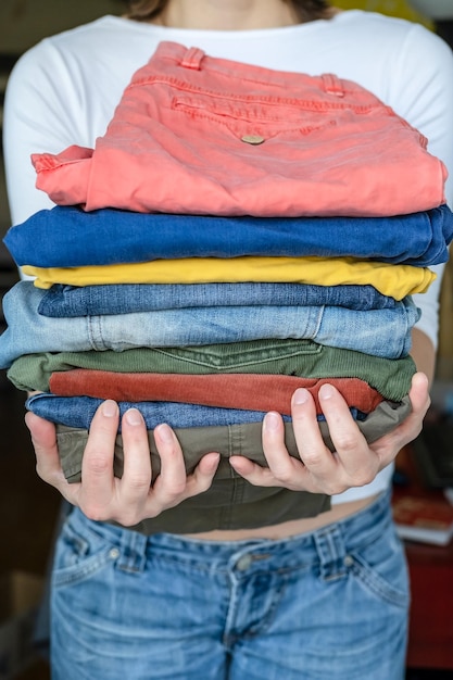 Main féminine tenant un pantalon et un jean soigneusement pliés aux couleurs vives après le lavage dans la buanderie