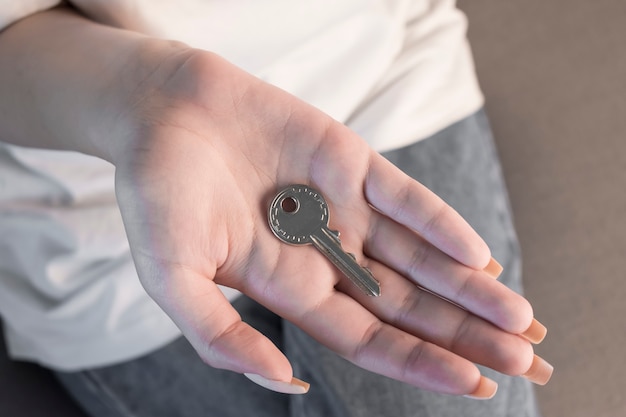 Main féminine tenant un porte-clés en forme de maison.