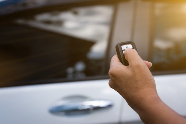 Photo main féminine tenant et poussant la télécommande de la voiture pour verrouiller ou déverrouiller la voiture.