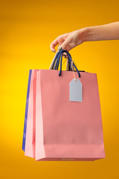 Main féminine tenant des sacs à provisions lumineux sur jaune