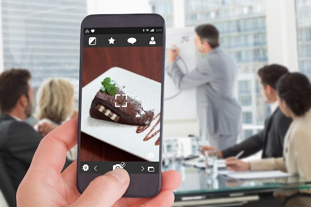 Photo main féminine tenant un smartphone contre la vue de face du gâteau au chocolat avec des fraises