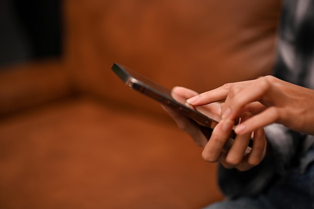 Une main féminine tenant un smartphone sur un salon moderne flou en arrière-plan