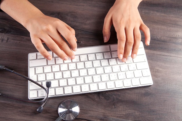 main féminine tenant un stéthoscope et tapant sur la vue de dessus du clavier d'un ordinateur portable