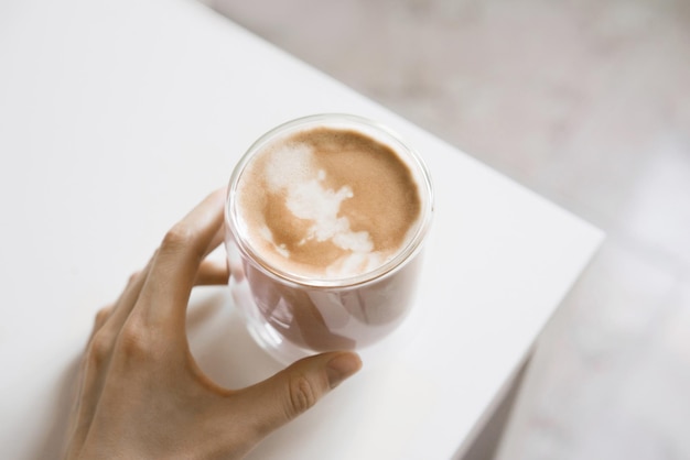 Photo main féminine tenant une tasse de café fait maison. cappuccino au lait. mise au point sélective