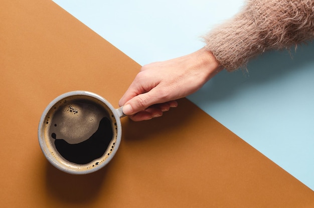 Main féminine tenant une tasse de café sur un fond bleu et marron