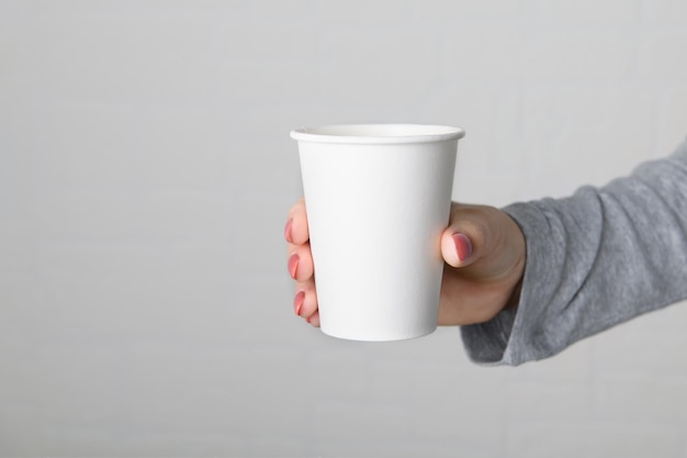 Main féminine tenant une tasse de papier à emporter vide vide sur fond de mur gris neutre