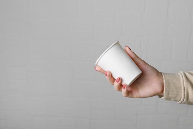 Main Féminine Tenant Une Tasse De Papier à Emporter Vide Vide Sur Fond De Mur Gris Neutre