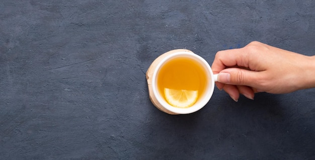 Main féminine tenant une tasse de thé avec vue de dessus de citron sur un fond de pierre sombre