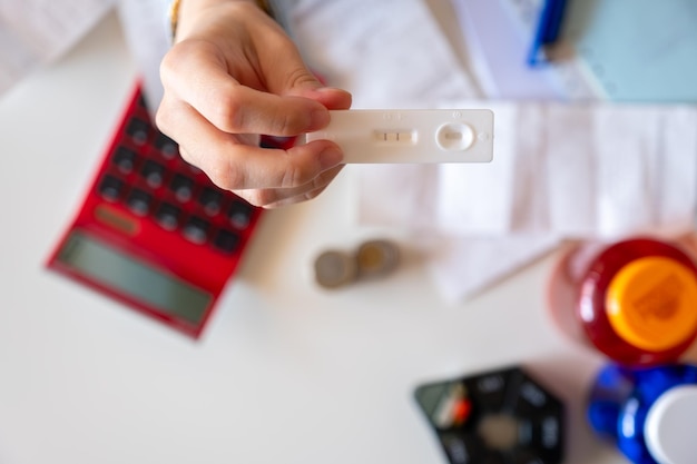 Main féminine tenant des tests de grossesse avec des reçus et une calculatrice en arrière-plan pour montrer le concept des coûts de la grossesse