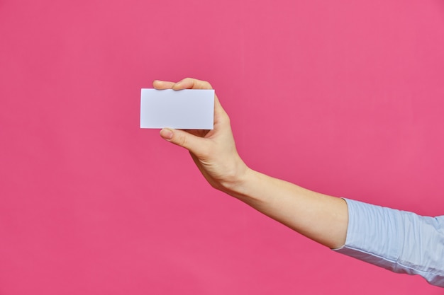 La main féminine tendue montre une carte blanche sur fond rose. Copiez l'espace.