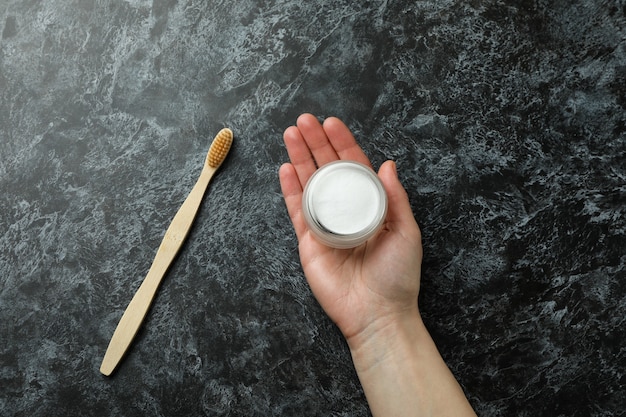 Main féminine tenir la poudre de dent sur fond noir smokey avec brosse à dents