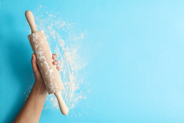 Main féminine tenir le rouleau à pâtisserie sur fond bleu