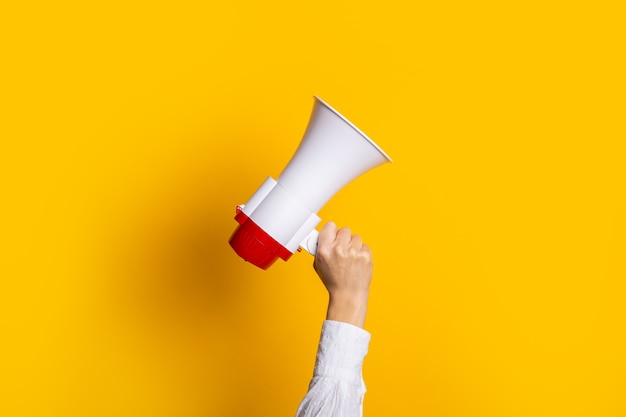 La main féminine tient un blanc avec un mégaphone rouge sur fond jaune