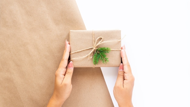 Main féminine tient une boîte-cadeau avec une branche d'arbre de Noël