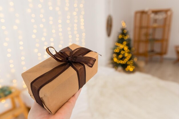 La main féminine tient un cadeau décoré arbre de Noël flou enveloppé présent célébrant et donnant le conceptNoël zéro déchet Boîte-cadeau emballée dans du papier décoré de dentelle et de ficelle