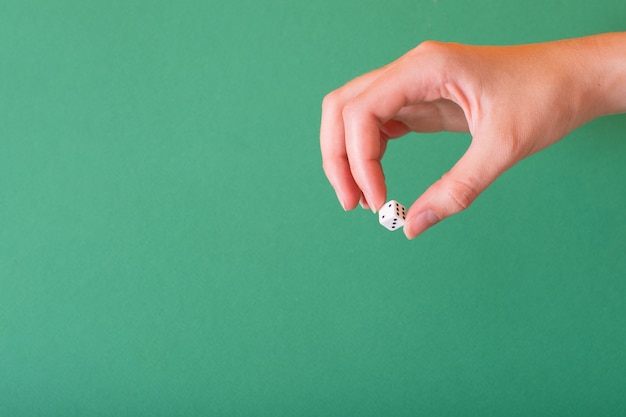 La main féminine tient un dé blanc sur fond vert. Idée pour le jeu, le casino, les jeux de dés.