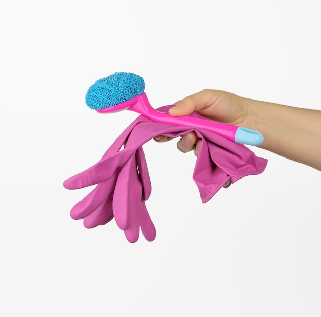 Main féminine tient des gants de nettoyage roses et une brosse sur fond blanc, gros plan