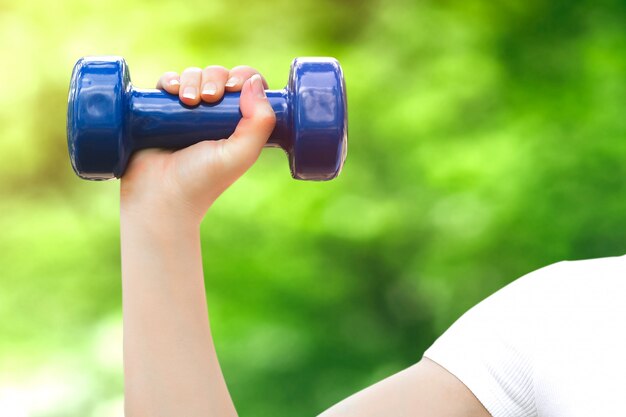 Une main féminine tient un haltère bleu