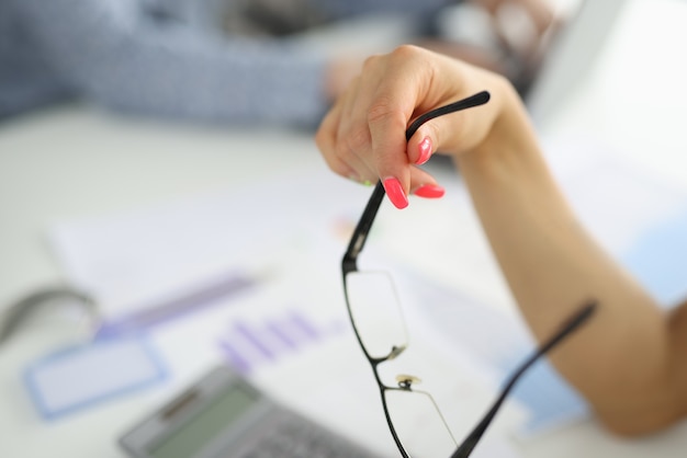 La main féminine tient des lunettes sur le bureau au bureau.